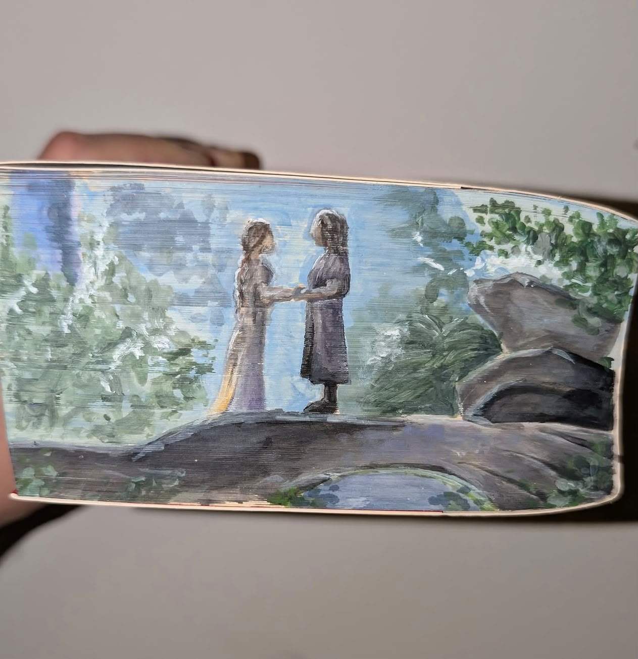 Fore-edge painting of Aragorn and Arwen holding hands on a stone bridge in Rivendell, surrounded by soft green trees.
