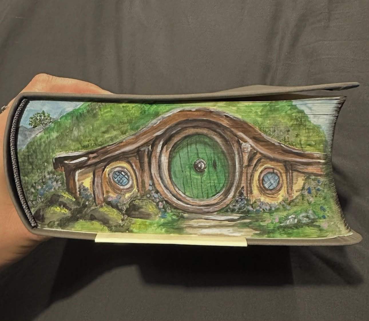 Fore-edge painting of Bag End, Bilbo’s round green door set into the grassy hill, with round windows and flowers along the path.