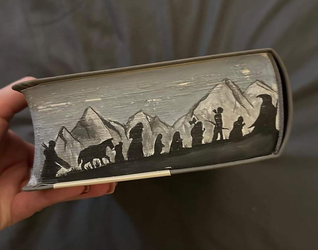 Fore-edge painting of the Fellowship of the Ring and Bill the pony in silhouette, walking beneath the grey, snow-capped Misty Mountains.