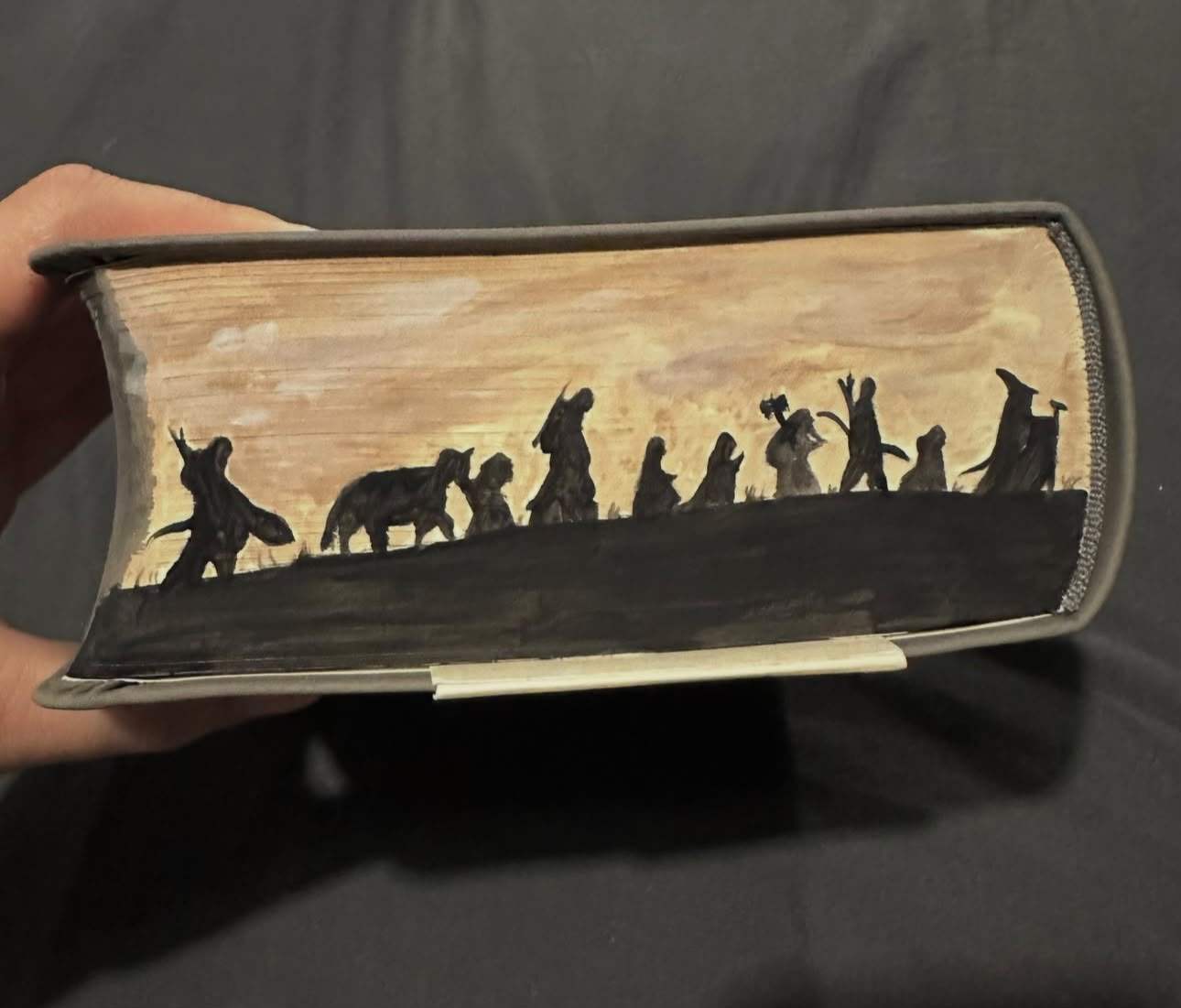 Fore-edge painting of the Fellowship of the Ring and Bill the pony in black silhouette, walking a ridge against a golden sky.