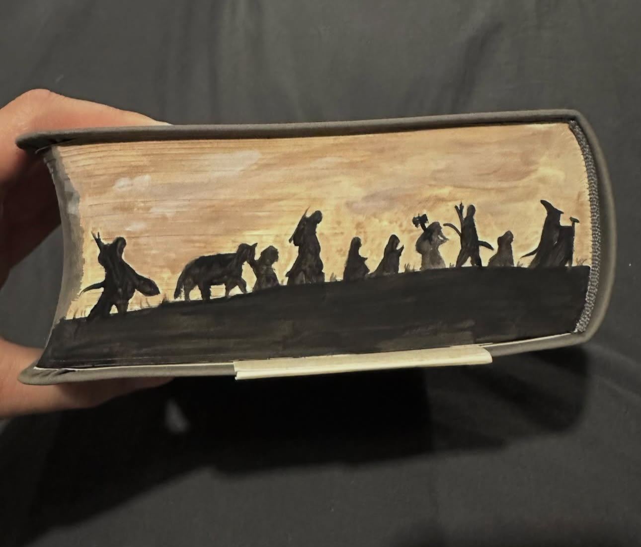 Fore-edge painting of the Fellowship of the Ring and Bill the pony in black silhouette, walking a ridge against a golden sky.