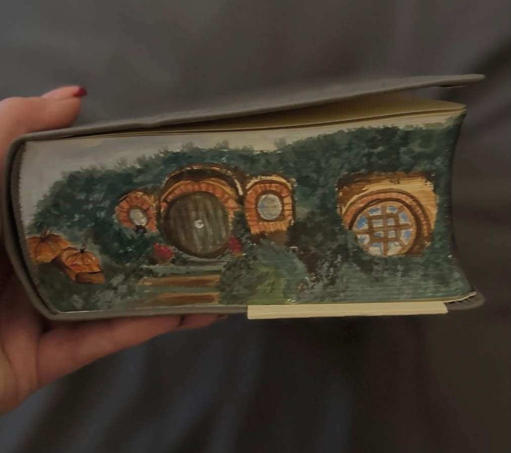 Fore-edge painting of hobbit holes in Hobbiton with round doors and windows, and orange pumpkins in the garden.